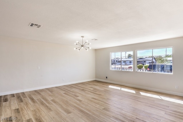 empty room featuring baseboards, visible vents, an inviting chandelier, a textured ceiling, and light wood-type flooring