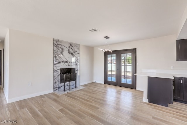 unfurnished living room with light wood-style flooring, a fireplace, visible vents, baseboards, and french doors