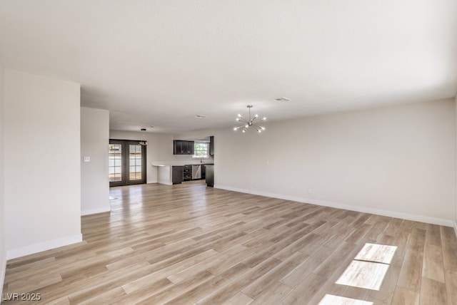 unfurnished living room featuring light wood finished floors, baseboards, a notable chandelier, and french doors