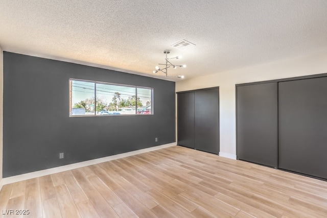 unfurnished bedroom featuring light wood finished floors, visible vents, baseboards, two closets, and a notable chandelier