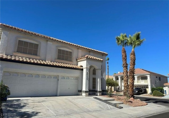 mediterranean / spanish house with an attached garage, a tiled roof, concrete driveway, and stucco siding