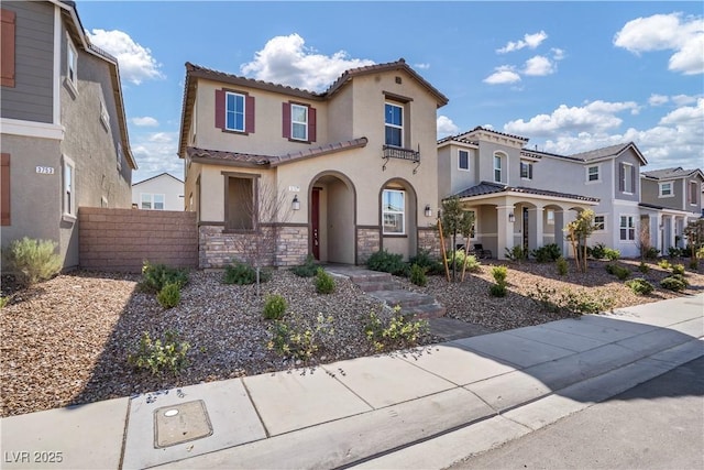 mediterranean / spanish-style home with stucco siding, fence, a residential view, stone siding, and a tiled roof