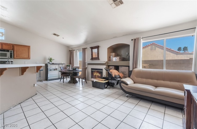 living area with lofted ceiling, visible vents, a tile fireplace, and light tile patterned floors