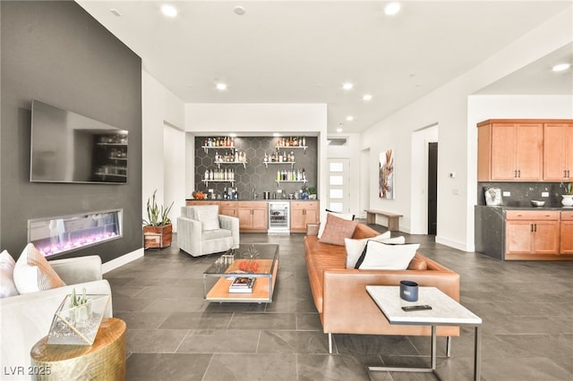 living room featuring wine cooler, indoor wet bar, recessed lighting, a glass covered fireplace, and baseboards