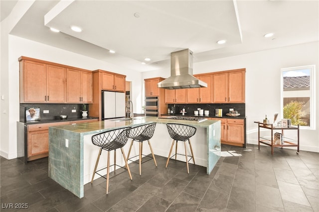 kitchen with island range hood, an island with sink, dark countertops, a breakfast bar area, and freestanding refrigerator