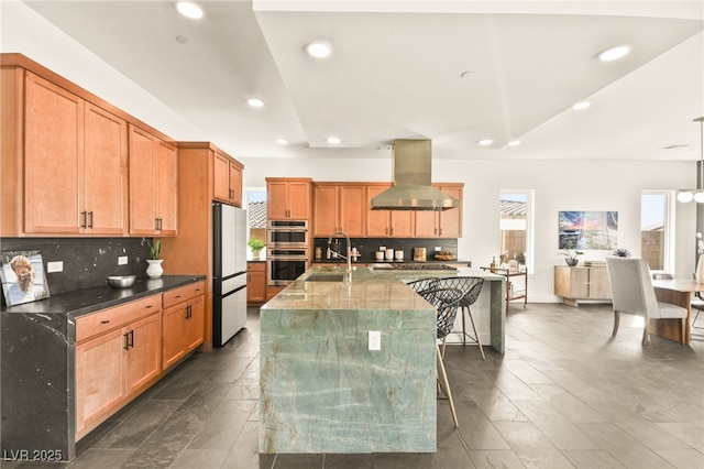 kitchen with decorative backsplash, appliances with stainless steel finishes, a kitchen breakfast bar, island exhaust hood, and a sink