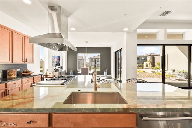 kitchen featuring tasteful backsplash, island range hood, dark stone counters, and a sink