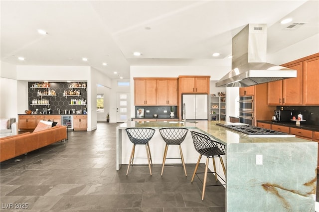 kitchen with tasteful backsplash, visible vents, island range hood, open floor plan, and stainless steel appliances