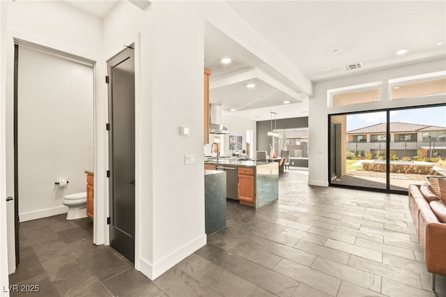 interior space featuring visible vents, dishwasher, open floor plan, wall chimney range hood, and a sink