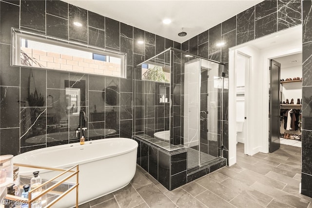 bathroom featuring a stall shower, a freestanding tub, a walk in closet, and tile walls