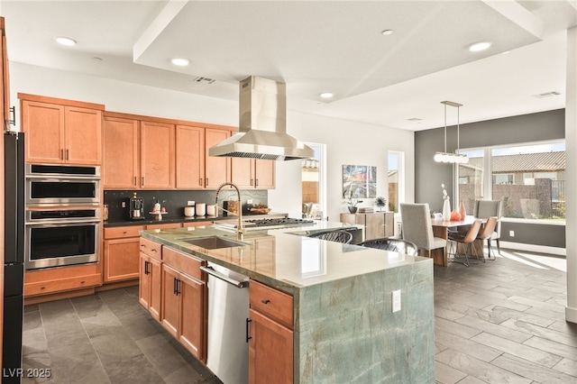 kitchen featuring a center island with sink, island exhaust hood, stainless steel appliances, pendant lighting, and a sink