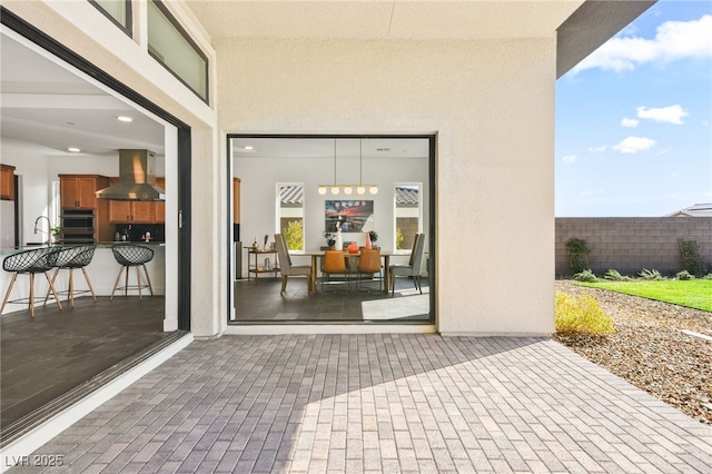 entrance to property featuring a patio area, fence, a sink, and stucco siding