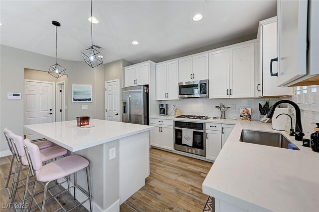 kitchen with a sink, backsplash, a center island, light wood-style floors, and appliances with stainless steel finishes