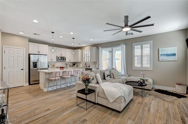 living room featuring visible vents, baseboards, ceiling fan, and light wood finished floors