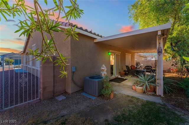 view of side of home with fence, central AC unit, and stucco siding