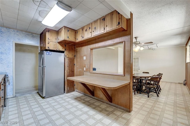 kitchen with wallpapered walls, brown cabinets, freestanding refrigerator, light countertops, and light floors