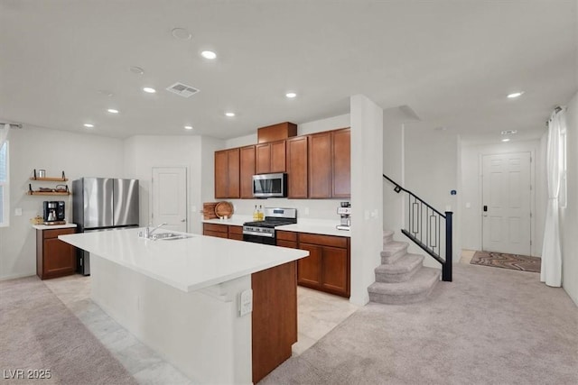 kitchen featuring appliances with stainless steel finishes, light countertops, a kitchen island with sink, and light carpet