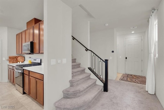 interior space featuring light carpet, stainless steel appliances, light countertops, and brown cabinets