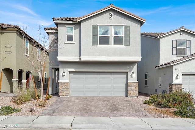 mediterranean / spanish-style house featuring an attached garage, a tile roof, stone siding, decorative driveway, and stucco siding