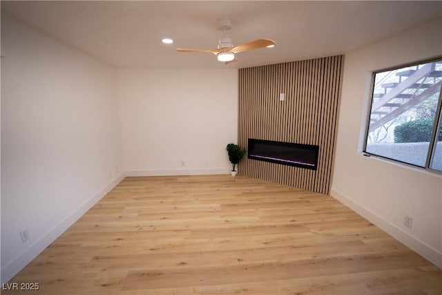 interior space featuring baseboards, a ceiling fan, a glass covered fireplace, light wood-style flooring, and recessed lighting