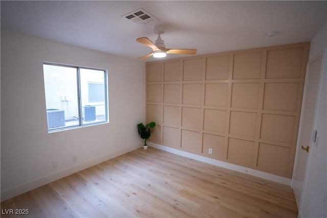 empty room with visible vents, baseboards, ceiling fan, light wood-style flooring, and a decorative wall