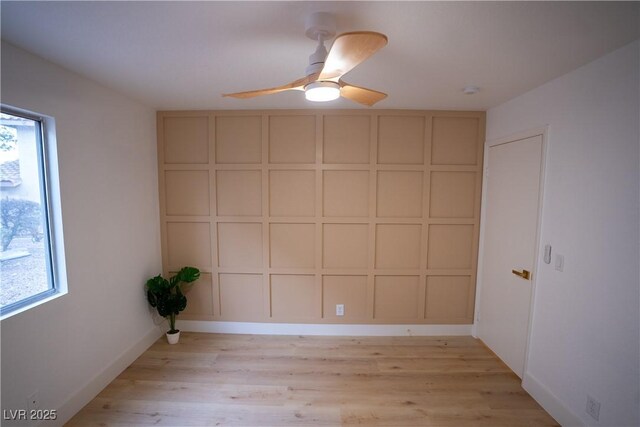 empty room with light wood-style floors, a decorative wall, and a ceiling fan