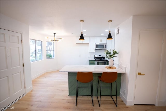 kitchen with stainless steel appliances, white cabinetry, light wood-style flooring, and a kitchen bar