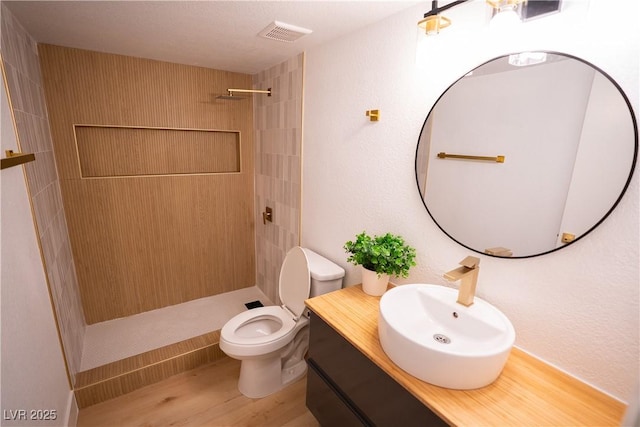 full bathroom with a stall shower, visible vents, toilet, wood finished floors, and vanity