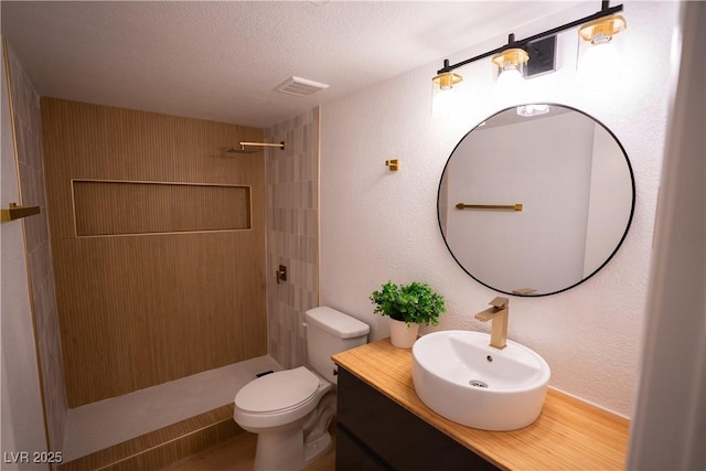 bathroom with a textured wall, toilet, a stall shower, a textured ceiling, and vanity