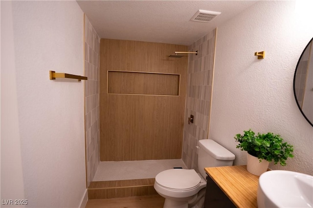 bathroom featuring visible vents, a textured wall, toilet, a stall shower, and a textured ceiling