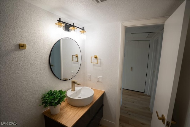 bathroom with a textured wall, vanity, and wood finished floors