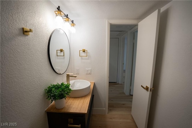 bathroom with vanity, baseboards, wood finished floors, and a textured wall