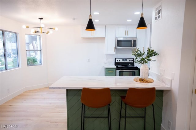 kitchen with appliances with stainless steel finishes, a breakfast bar, light stone counters, light wood-style floors, and white cabinetry