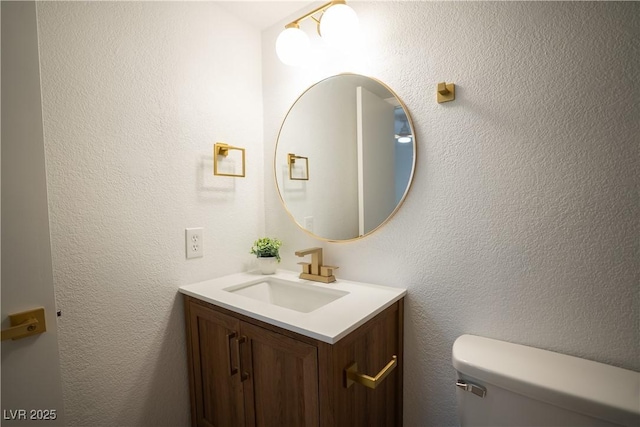 half bath with toilet, a textured wall, and vanity