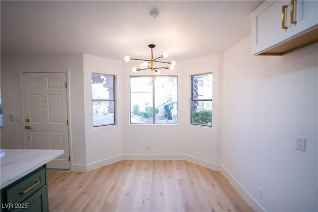 unfurnished dining area featuring a chandelier, light wood finished floors, and baseboards