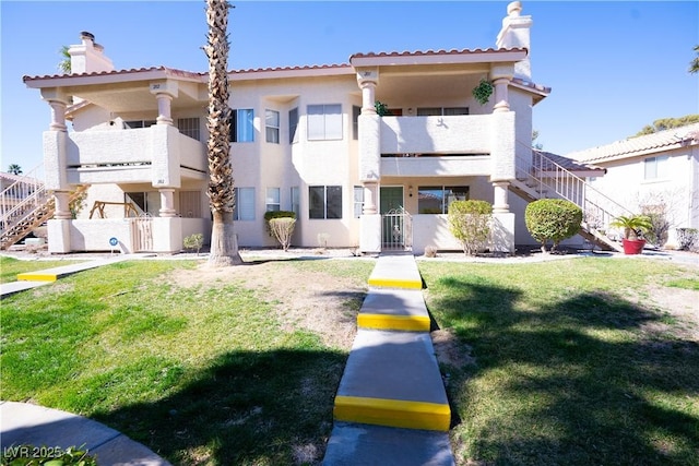 view of front of home with stairs, a front lawn, a chimney, and stucco siding