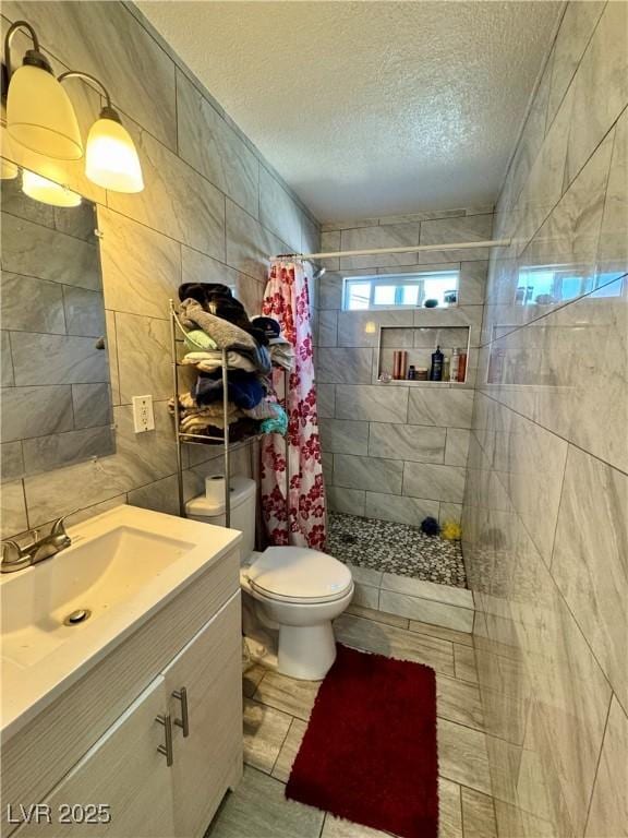 full bath featuring a textured ceiling, toilet, vanity, tile walls, and a stall shower