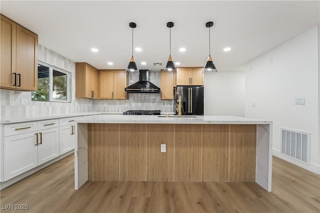 kitchen featuring high end black refrigerator, visible vents, white cabinetry, light countertops, and wall chimney exhaust hood