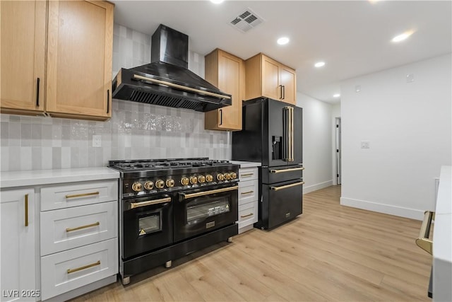 kitchen featuring visible vents, light countertops, light brown cabinetry, wall chimney range hood, and black appliances