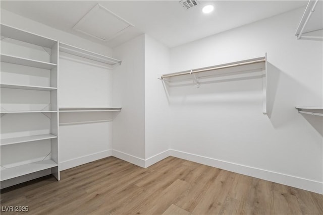 spacious closet with attic access, visible vents, and wood finished floors