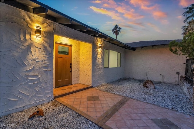 view of exterior entry featuring stucco siding and a patio