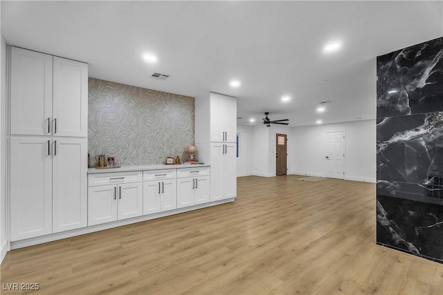 kitchen with light wood-style flooring, visible vents, white cabinets, light countertops, and wallpapered walls