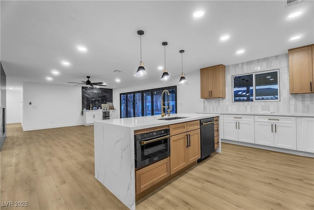 kitchen featuring a center island with sink, open floor plan, white cabinetry, a sink, and black oven