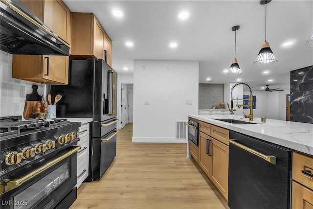 kitchen featuring a sink, hanging light fixtures, black appliances, wall chimney exhaust hood, and light wood finished floors