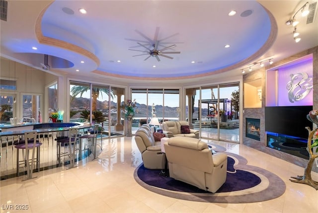 living room featuring a tray ceiling, a fireplace, recessed lighting, and ceiling fan