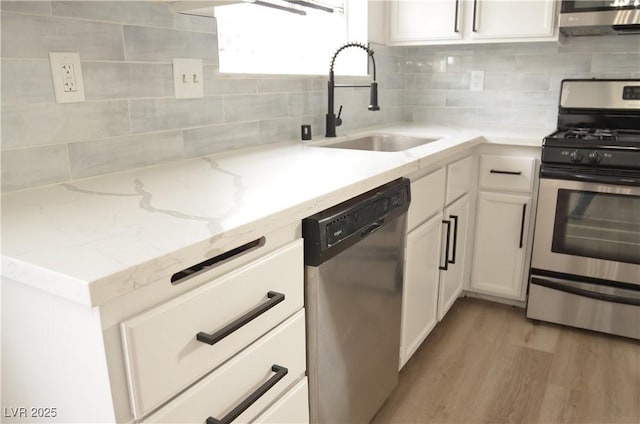 kitchen featuring light stone counters, decorative backsplash, appliances with stainless steel finishes, white cabinets, and a sink