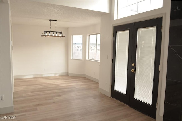 entrance foyer featuring light wood-type flooring, baseboards, a textured ceiling, and french doors