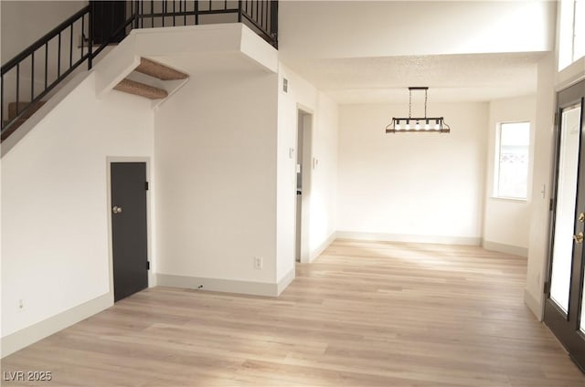 hall featuring stairs, light wood finished floors, a towering ceiling, and baseboards