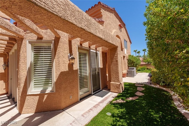 view of property exterior featuring central air condition unit, a tile roof, a patio, and stucco siding