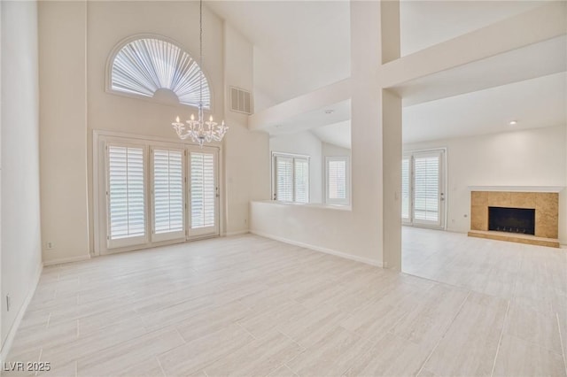 unfurnished living room with wood finish floors, visible vents, a towering ceiling, a tiled fireplace, and a chandelier